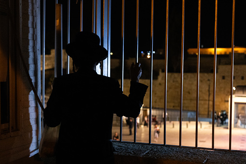 Back view of Israeli, Orthodox Jewish man looking through gate at Western Wall during the month of Yom Kippur at midnight