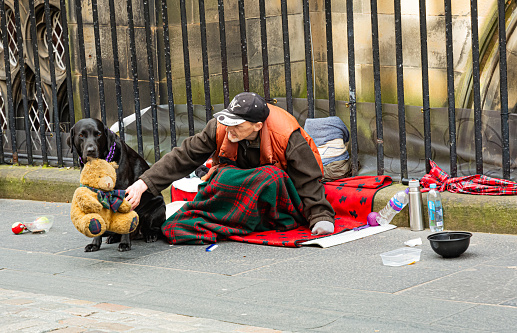 Local homeless man and his pet dog sits on the pavement along the Royal Mile in Edinburgh - a popular tourist destination.\nEditorial image of city life in the capital city.\nEdinburgh, Scotland, United Kingdom - September 11th 2019: