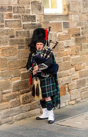 Man in traditional dress with tartan kilt playing the bagpipe whilst walking along the Royal Mile in Edinburgh, Scotland. \n10th September 2019