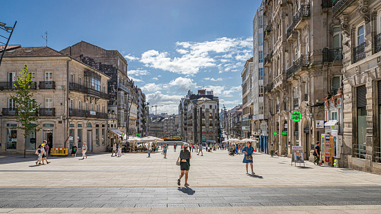 Vigo, Spain. August 3rd, 2023. The central square of the city with some random tourists and local people. Businesses and a restaurant terrace on bright summer day.