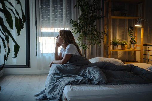 Depressed mid-adult woman sitting in bed, suffering from insomnia