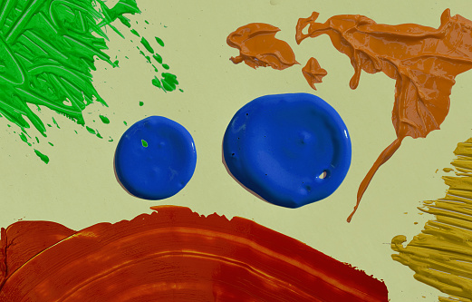 multicolored blotches of thick ink on a cream color surface. screen printing inks in blue, green, orange, yellow and red