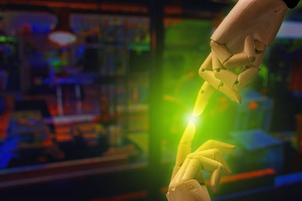 Wooden mannequin hands, index fingers approaching each other. In the background, a shaded Bulurlu laboratory emits green light from the point where the fingers meet.