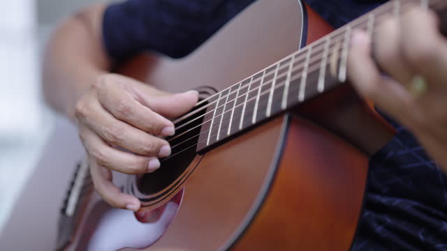 Close up man plays with his fingers on a acoustic guitar for hobby and practice.