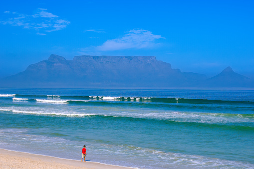 Cape Town, South Africa - April 22, 2007: A lone young boy on the sandy beach near Milnerton. In the far background is Table Mountain almost covered in fog. It is an ideal day for swimming in the Atlantic Ocean. The image was shot in the afternoon sunlight.