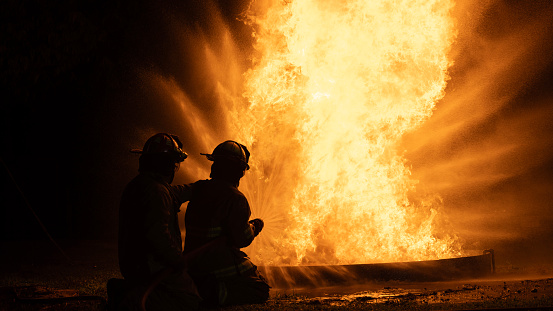 Two-man firefighters use Twirl water fog-type fire extinguishers to fight the fire flame from gas exposure to prevent the fire from spreading out. Firefighter and industrial safety concept.