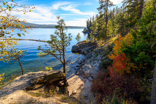 Autumn view of a small sandy beach and rocky cove on Tubbs Hill, a hiking trail loop along Lake Coeur d'alene in the downtown area of the resort town of Coeur d'Alene, Idaho USA. Coeur d’Alene is a city in northwest Idaho. It’s known for water sports on Lake Coeur d’Alene, plus trails in the Canfield Mountain Natural Area and Coeur d’Alene National Forest. McEuen Park offers a grassy lawn and a trailhead for adjacent Tubbs Hill. The lakeside City Park & Beach includes picnic areas and a playground.