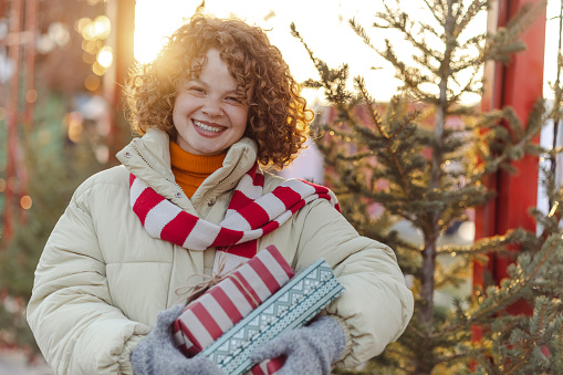 Happy beautiful woman with red hair in warm clothing holding Christmas presents and looking at the camera