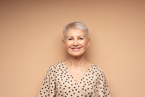 Elderly smiling beautiful woman with a short pixie haircut in a beige dress