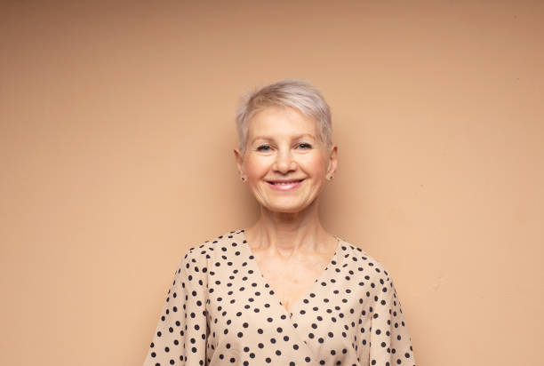 Elderly beautiful woman with a short pixie haircut in a beige dress stock photo