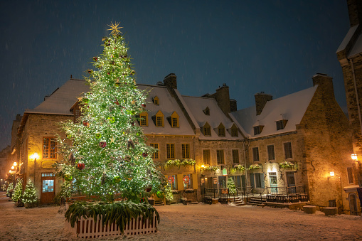 Christmas tree and winter holiday decorations in Place Royale on a snowy night, lower town in Old Quebec, Quebec City, Canada. Photo taken during a midnight walk in December 2022.