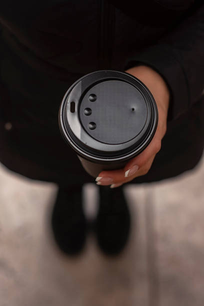 The girl is holding a glass of coffee with a plastic lid in her hand.