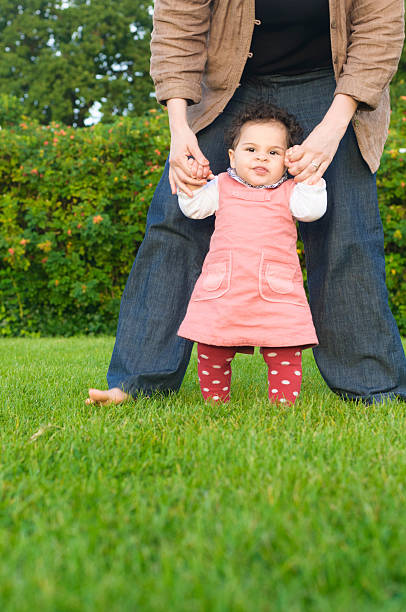 ребенок девочка, что дел�ает первые шаги в своей матери - babies and children cheerful low angle view vertical стоковые фото и изображения