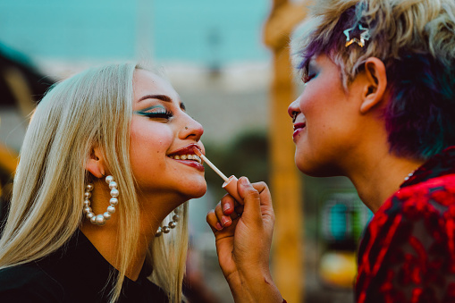 Young woman applying lipstick on her friend lips. Friendship and beauty concept.