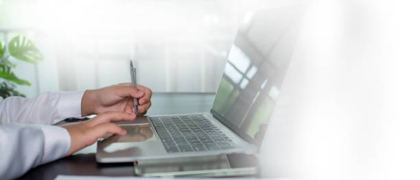 istock Businessman holding a pen and using a computer to work sits in a modern office with copy space. 1753286035