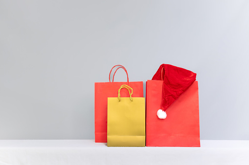 Red and yellow shopping bags on a gray background, with a Santa hat peeking out from one. Ideal for Christmas shopping promotions and ads