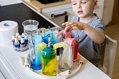 Cute baby boy learning mixing different colors with water and paint in containers. Early development
