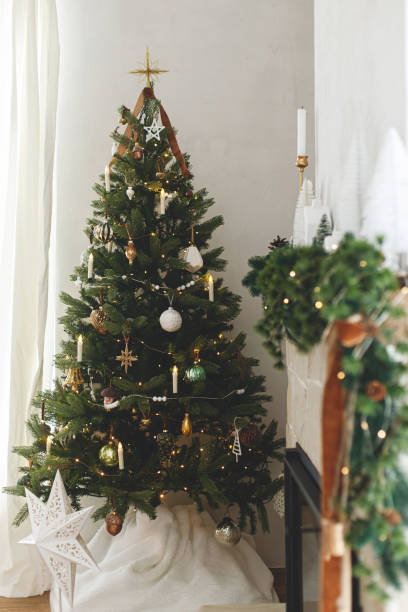 istock Stylish decorated christmas tree with vintage baubles  and modern decor on fireplace mantel with bells and ribbon. Modern christmas scandinavian living room. Atmospheric christmas eve 1753383487