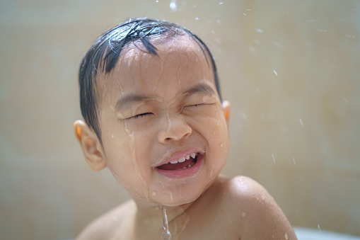 Adorable Asian little boy taking a bath and making a funny face when his mother pours water on his head