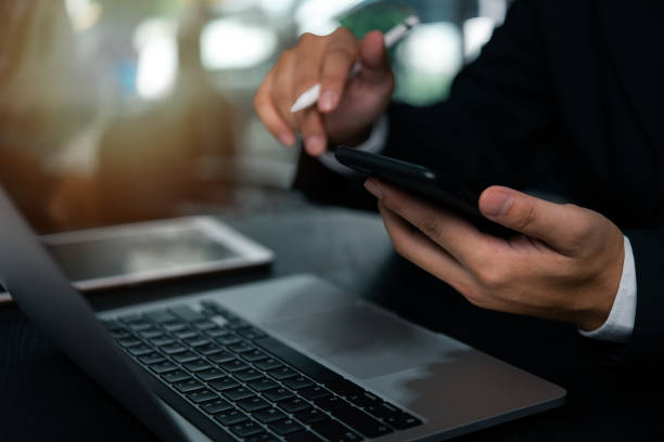 istock Businessman hand holding mobile smartphone on a table with a laptop at office. 1753435950