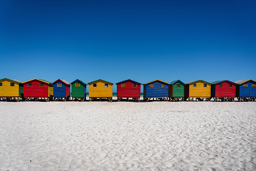 Muizenberg Beach close to Cape Town. Colourful beach with beach huts side by side in a row on the white sandy beach of Muizenberg under blue cloudless summer sky. Muizenberg Beach, Muizenberg, Cape Town, South Africa, Africa