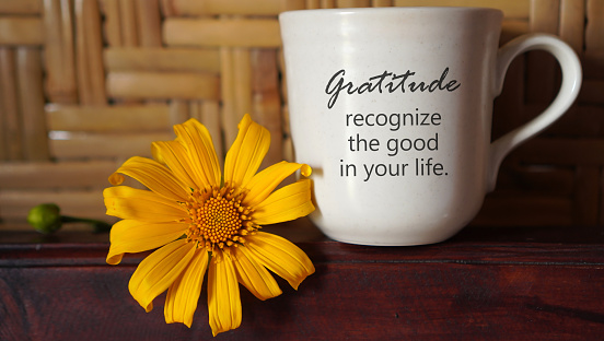 Grateful inspirational quote on a coffee cup - Gratitude recognize the good in your life. With beautiful yellow little sunflower on the table and brown bamboo wall background. Gratitude concept.
