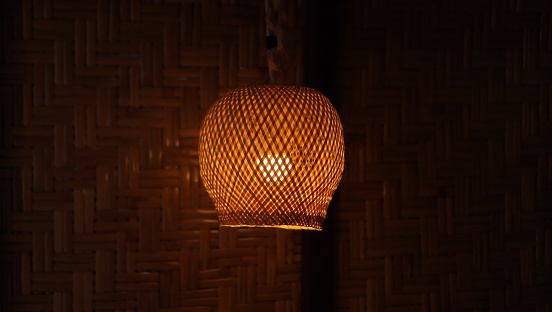 Bamboo lampshade light at night. Natural handmade wooden lamp hanging in the bedroom with warm low light on dark background.