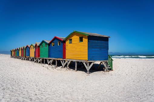 Muizenberg Beach close to Cape Town. White sandy beach with colourful beach huts side by side in a row on the famous white sandy beach of Muizenberg under blue cloudless summer sky. Muizenberg Beach, Muizenberg, False Bay, Cape Town, South Africa, Africa