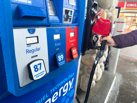 Calgary, Alberta, Canada. Oct 23, 2023.Various types of gasoline available with a person returning the nozzle to the gas station pump.