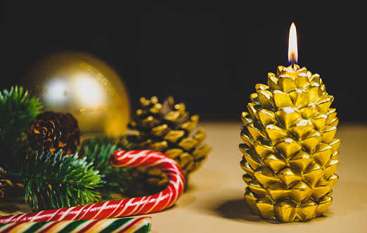 Christmas candle in gold color in the shape of a pine cone and New Year decorations around. Night.