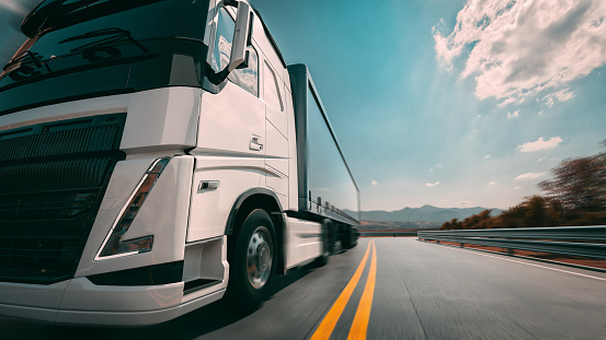A large white truck is traveling on the highway in a left-to-right direction. The sky behind is bright blue.3d, rendering, illustration,-