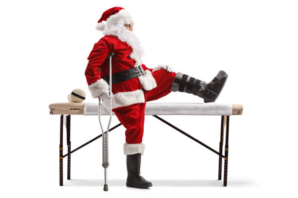 photo de profil du père noël avec une attelle et une béquille assis sur un lit médicalisé - christmas crutch holiday christmas decoration photos et images de collection