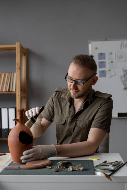 istock Archeologist works in office, researching discovered ancient civilization cultural artifact, cleaning with brush. 1753597655