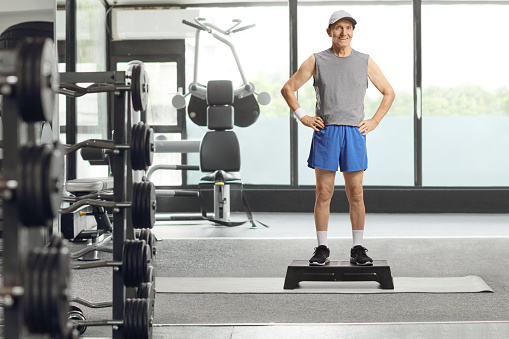 Full length portrait of an elderly man in sportswear standing on a step aerobic platform at a gym