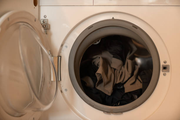 istock White built in washing machine with dirty clothes inside and open glass door. 1753621640