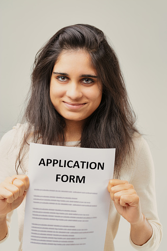 With an 'APPLICATION FORM' held prominently, an Indian young woman's expression speaks of ambition. Her dark tresses and soft smile contribute to a portrait of hope and anticipation