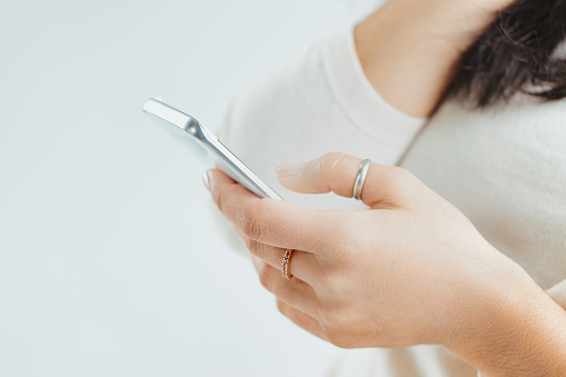 In sharp contrast to the soft background, a woman's hand grips a sleek smartphone, with her nails and rings in clear view