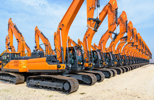 Tens of brand new orange caterpillar excavators lined up in a row outdoors under a stormy sky.