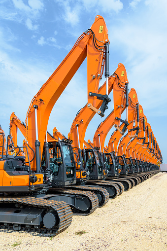 Tens of brand new orange caterpillar excavators lined up in a row outdoors under a stormy sky.