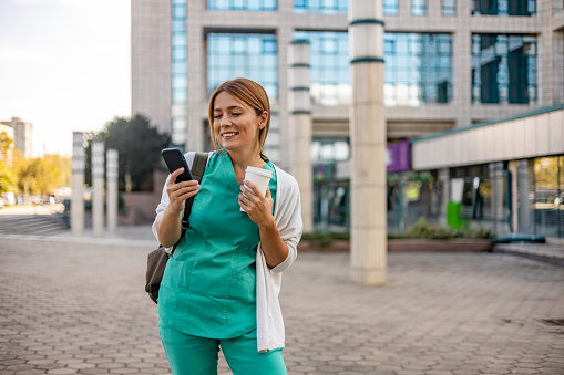 Young female nurse using her smartphone while standing.