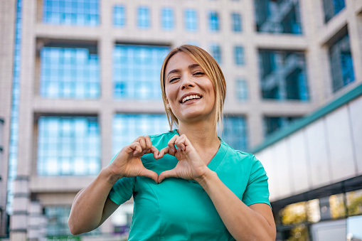 Attractive young nurse standing alone outside and making a heart shaped gesture