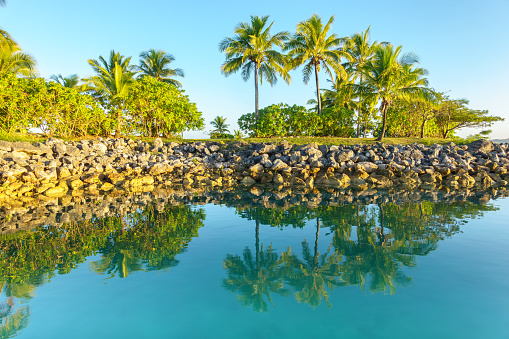 Sunrise illuminates the landscape and mirror image reflected in bay in tropical Fiji.