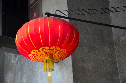 A hanging red lantern with Chinese characters in yellow. Red is an auspicious color for Chinese and drives away bad luck. Chinese lanterns originally had a practical use but are now used more for decorative and festive purposes. This lantern was hanging outside a house in Singapore Chinatown.