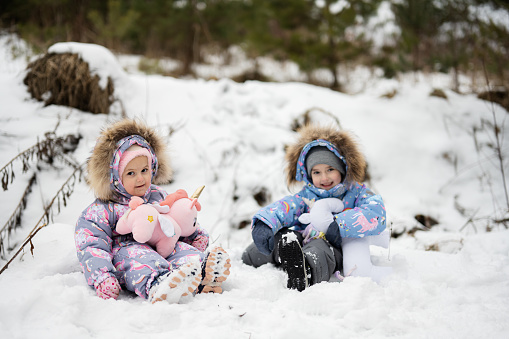 Two sisters in winter forest with stuffed unicorn toys.