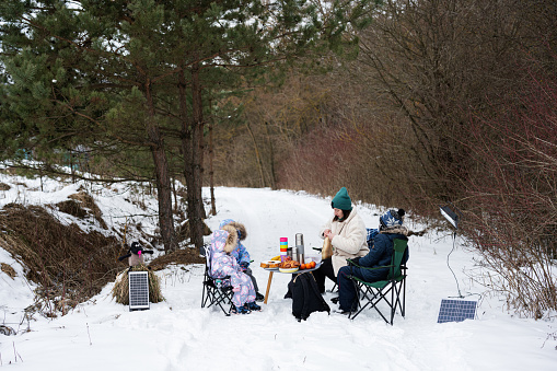 Young woman with children in winter forest on a picnic. Mother and three kids.