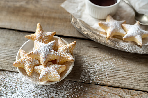 Puff pastry star shaped food bites dusted with powdered sugar on wooden table angle view