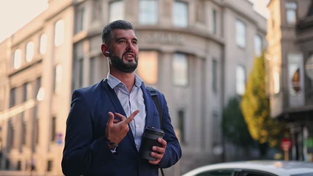 Mid Adult Businessman Having A Phone Call Using Headphones And Drinking Coffee In The City