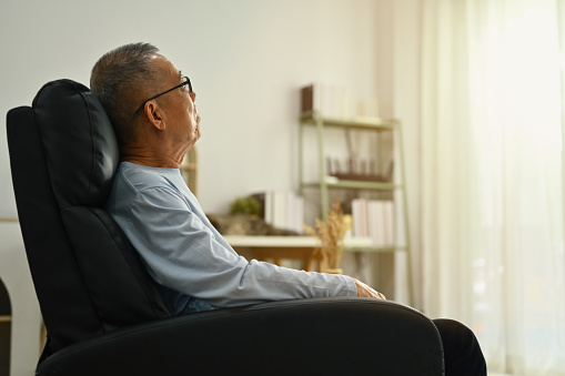 Pensive mature man sitting on armchair in living room and looking in distance thinking or pondering.