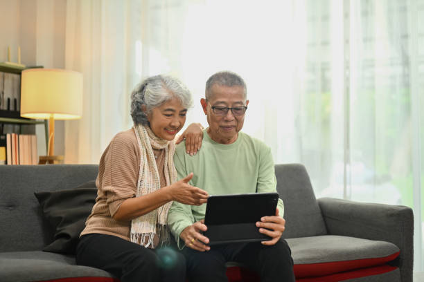 istock Happy retired spouses relaxing on sofa doing internet shopping and browsing internet in digital tablet 1753755504