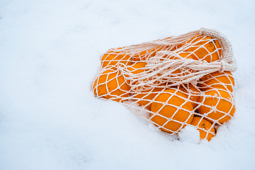 On snow, tangerines lie in wicker bag, cozily ensconced in their bag